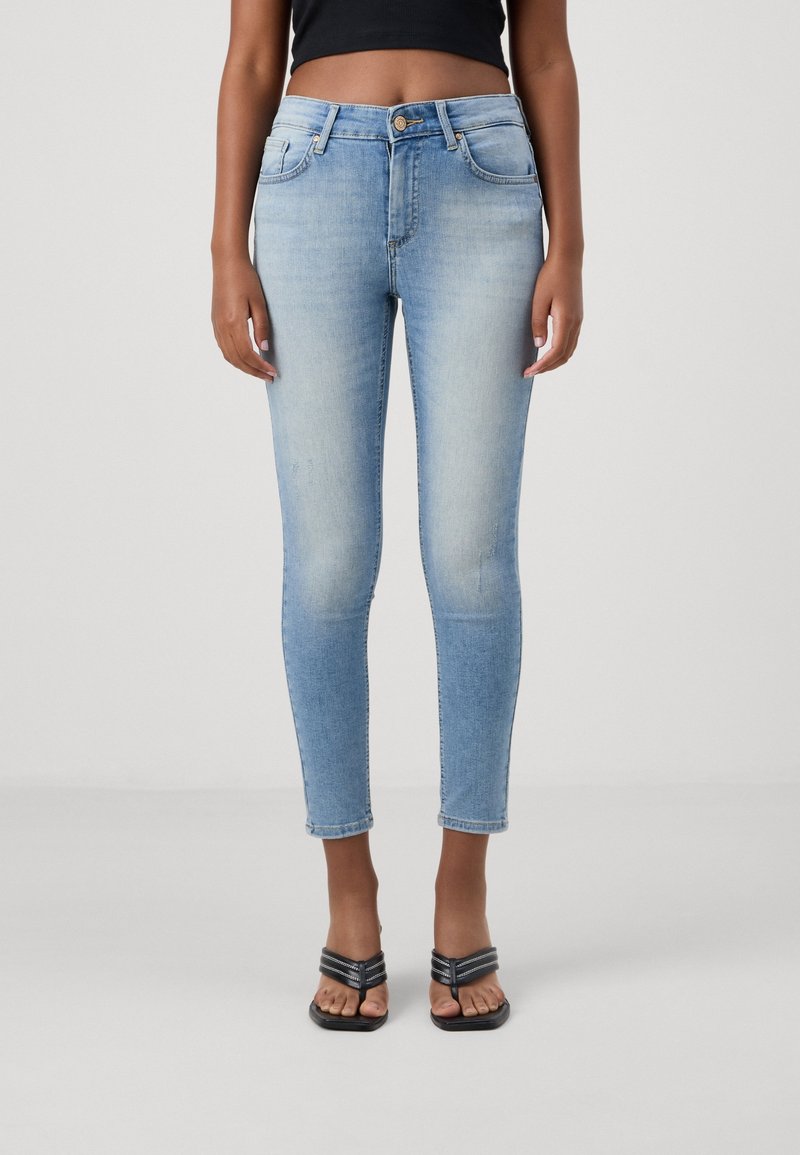Light blue skinny jeans with a high-rise waist, five-pocket design, and subtle fading. Paired with black strappy sandals.