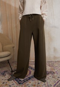 Breda ben, olivgröna byxor i mjukt tyg, med elastisk midja och dragsko, sidofickor och en avslappnad passform.