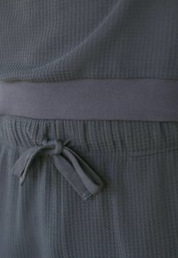 Grau strukturierten Stoff mit einem Karomuster, ausgestattet mit einem elastischen Bund und Kordelzug. Weiches, leichtes Material.