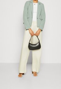 Světle zelený blazer, bílý top, krémové široké kalhoty a malá černá kabelka. Celý outfit doplňují páskové bílé sandály.