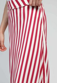 Jupe rayée rouge et blanche en tissu, avec une fente sur le côté. Les rayures sont verticales et de largeur égale. Main positionnée sur le tissu.