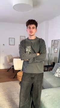 Γκρίζο πουκάμισο με μακριά μανίκια και λευκό γραφικό μπροστά, σε συνδυασμό με σκούρες φαρδιές τζιν. Δωμάτιο σε ουδέτερες αποχρώσεις με ανοιχτόχρωμα ξύλινα έπιπλα.