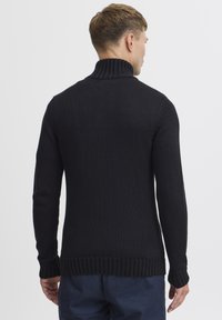 Svart stickad tröja med hög krage, ribbade ärmslut och nederkant. Texturen är fin och ger både värme och en åtsittande look.