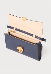 Navy leather handbag with gold circular hardware, interior pocket, and a light tan lining. Features a detachable strap for versatility.