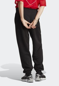 Black sweatpants with a relaxed fit, elastic waistband, and ribbed cuffs. Worn with black sneakers and a red top.