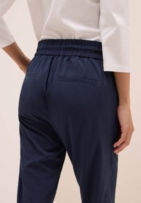 Pantalones de cintura elástica en azul marino con una textura suave, que cuentan con dos bolsillos traseros y un corte relajado. La parte superior es de un color claro y de manga larga.