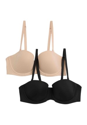 Donna che indossa un reggiseno nero senza spalline con spalline removibili e slip neri a vita alta, che guarda verso il basso con una mano sul fianco.