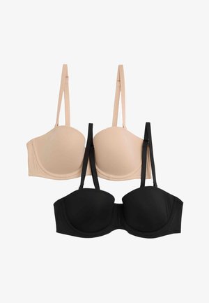 Kobieta w czarnym biustonoszu bez ramiączek z odpinanymi paskami i wysokich czarnych majtkach, patrząca w dół, z jedną ręką na biodrze.