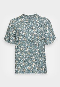 Top floreale a maniche corte in teal con fiori bianchi e gialli. Scollatura rotonda e maniche leggermente svasate. Tessuto leggero con una consistenza liscia.