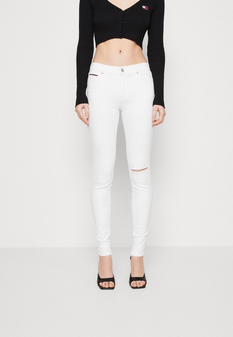 Jeans skinny blancos con un detalle rasgado en la rodilla derecha. Combinados con un top corto de canalé negro con cierre de botones. Tacones negros de punta abierta.