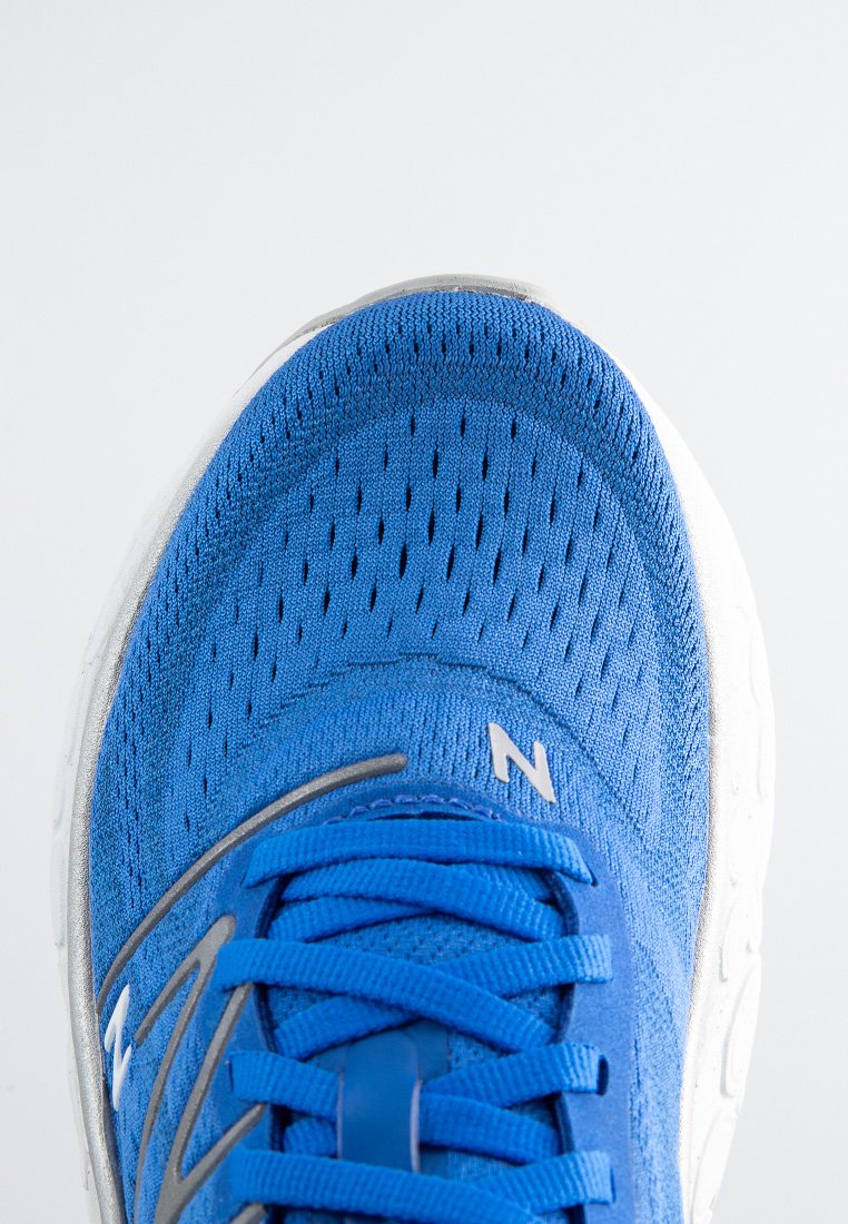 Zapatilla deportiva azul con un upper de malla texturizada, acentos plateados en contraste y una suela blanca acolchada. Incluye cordones planos y detalle de marca.