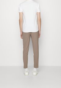 T-shirt bianca a maniche corte abbinata a pantaloni beige slim-fit e sneakers bianche. Il look è casual con una silhouette pulita.