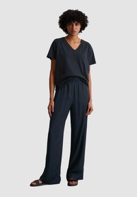 Dark gray V-neck t-shirt, relaxed fit, paired with dark pants featuring an elastic waistband. Flat sandals complete the outfit.