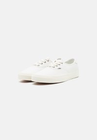 Baskets en toile blanche avec une semelle en caoutchouc, un bout rond et un laçage à l'avant. Présentent une surface texturée et un logo discret sur le côté.