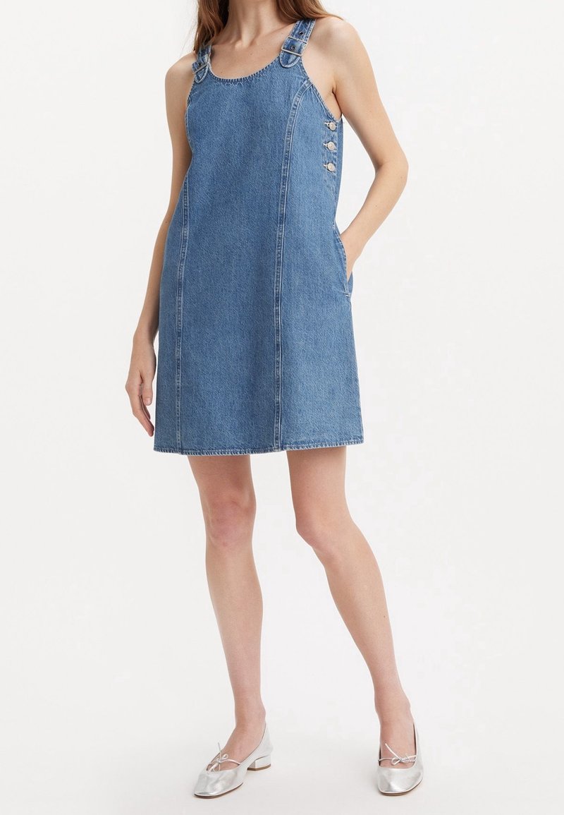 Denim overallklänning med justerbara remmar, sidoknappar och fickor. A-linjeform i ljusblå tvätt. Slät textur.