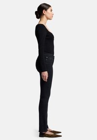 Schwarzes geripptes Langarmoberteil kombinert mit hochtaillierten schwarzen Skinny-Jeans und spitzen Leopardenmuster-Ballerinas, seitlich betrachtet.