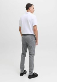 Pantalones chinos grises de corte ajustado, con bolsillos traseros con botones, combinados con una camiseta polo blanca y zapatos negros.