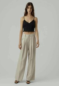 Top cropped preto com rendas, combinado com calças largas de cintura alta em bege. Modelo de pé sobre um fundo neutro.