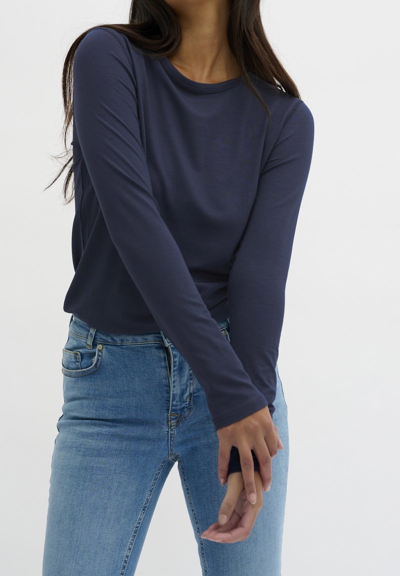 Marineblaues Langarmoberteil aus weichem, dehnbarem Stoff, kombiniert mit hellblauen Jeans aus Denim, die eine schmale Passform und einen Rundhalsausschnitt zeigen.