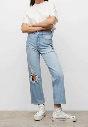 Lyseblå denimjeans med høj talje, vide ben og stort knærevne. Kombineret med en hvid cropped t-shirt og hvide højtop-sneakers.