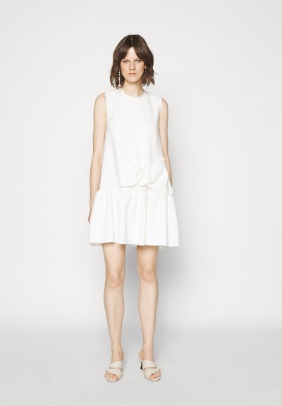 Bijela haljina bez rukava s lepršavim volanom na rubu i mašnom na struku. Glatka tkanina, jednostavan dizajn i bez vidljivih uzoraka.