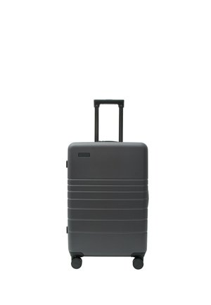 Dunkelgrauer Hartschalenkoffer mit horizontalen Rillen, vier Rollen und ausgezogenem schwarzem Teleskopgriff auf weißem Hintergrund.