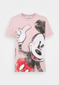 Camiseta rosa con un diseño gráfico audaz de un personaje de dibujos animados sonriente con un pulgar hacia arriba, colocado sobre un fondo salpicado.