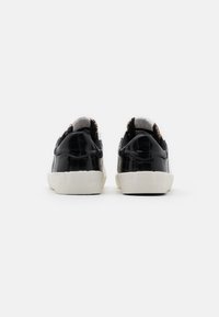 Sneakers in pelle verniciata nera con accenti bianchi, finitura testurizzata, punta tonda e suola in gomma. Dettagli ornamentali sul tallone.