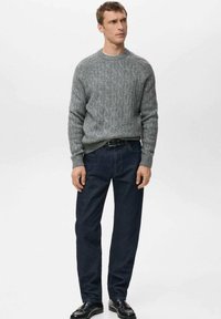 Szary sweter w sploty z okrągłym dekoltem, połączony z ciemnoniebieskimi prostymi dżinsami. Czarny pasek i eleganckie buty dopełniają strój.