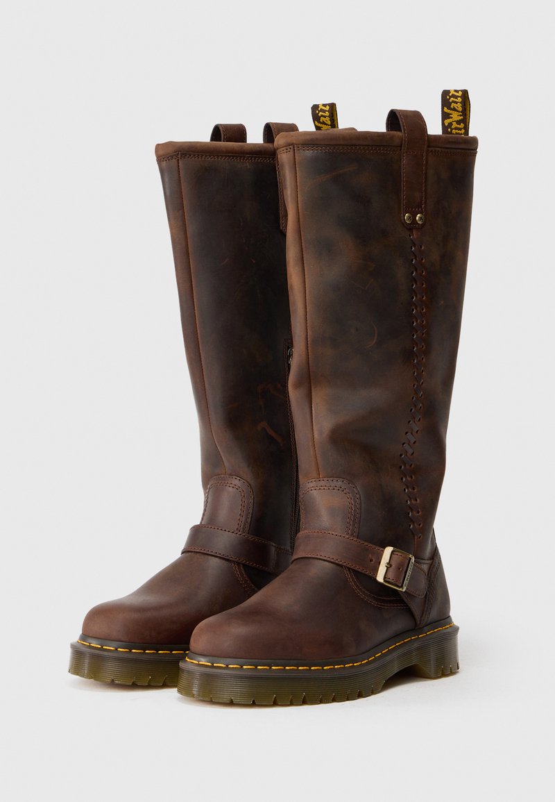 Braune Lederstiefel bis zum Knie mit seitlichem Reißverschluss, Schnallenriemen, gelber Naht und Lasche; strukturierte Oberfläche mit subtilen Farbvariationen.