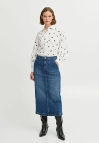 Weiße Bluse mit navyfarbenem Blättermuster, langen Ärmeln, Knopfverschluss vorne, kombiniert mit einem knielangen, dunkelblauen Jeansrock und schwarzen Stiefeln mit Absatz.