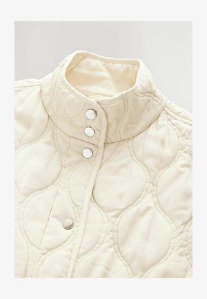 Gequilte ivoorkleurige jas met een hoge kraag en vier drukknoopjes. Beschikt over een zachte textuur en subtiele gebogen patronen door het hele jasje.