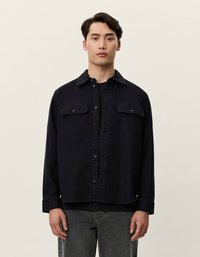 Σκούρο μπλε σακάκι με κουμπιά, δύο μπροστινές τσέπες, γιακά και χαλαρή εφαρμογή, συνδυασμένο με μαύρο τοπ και γ κρι τζιν. Στερεά υφή, casual σχέδιο.