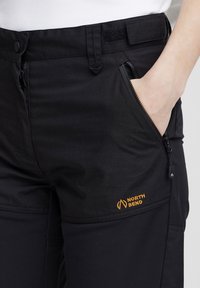 Čierne nohavice s vreckami na zips, textúrovanou tkaninou a oranžovým logom "NORTH BEND". Obsahujú patentku a zapínanie na suchý zips v páse.