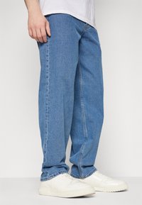 Light blue denim jeans with a relaxed fit, featuring a straight leg design and subtle stitching details, paired with white sneakers.