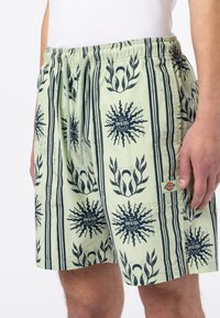 Hellgrüne Shorts mit einem grafischen Druck von Sonnenmotiven und Streifen; elastischer Bund; Logostick auf der Seite.