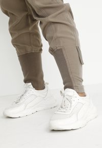 Vita sneakers med mesh- och läderdetaljer, parat med taupe tapered byxor med ribbad mudd och sydda accenter.