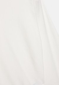 Valkoinen puuvillakangas, jossa on pehmeä rakenne, sileä pinta ja hienovarainen kiilto, näyttää kaarevan sauman yksityiskohtia.