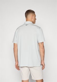 Πολο μπλούζα σε ανοιχτό γκρι χρώμα με υφαντό μοτίβο, διαθέτοντας το μαύρο λογότυπο της Nike στη βάση του λαιμού και κοντά μανίκια. Φοριέται με ανοιχτόχρωμες βερμούδες.