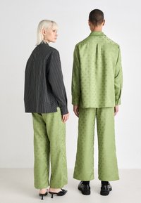 Črna prugasta majica, ohlapen kroj; zeleni bluzon s patternom in široke hlače; oboje iz teksturirane tkanine z diskretnimi detajli. Črna obuvala.