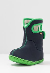 Czarny but z tkaniny z zielonymi wykończeniami i podeszwą, charakteryzuje się wodoodpornym designem, przeszyciami oraz pętelką do łatwego zakładania.