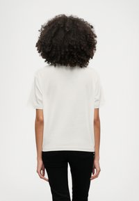 Biała bawełniana koszulka z krótkim rękawem, luźny krój i okrągły dekolt. Noszona z dopasowanymi czarnymi spodniami.