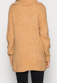 Cardigan beige oversize con trama a coste, colletto ampio e maniche lunghe. L'orlo è leggermente più lungo sul retro, con una finitura morbida.