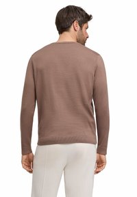Brauner Langarmpullover aus strukturiertem Stoff, mit rundem Halsauschnitt und geripptem Saum sowie Bündchen, kombiniert mit hellen Hosen.
