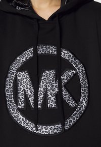Black hoodie featuring a large circular logo with a leopard print pattern and the letters "MK" in the center. Textured fabric and drawstrings.