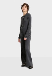 Grijs geribbeld gebreid twee-delige set met een coltrui met lange mouwen en knopen, en flared broek. Soepele textuur en een relaxte pasvorm.