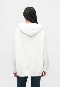 Biela oversized mikina s kapucňou a šnúrkou, dlhými rukávmi a rebrovanými manžetami. Mäkká textúra a voľný strih.