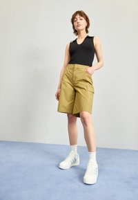 Cargo shorts i olivgrön bomull, med stora sidofickor; matchat med vita sneakers med blå detaljer och strumpor. En enkel, ren design.