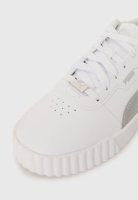 White athletic sneaker with a textured sole, featuring a smooth upper, lace closure, and a grey side panel with perforations and branding detail.
