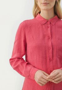 Lyserød linned skjorte med knaplukning, der har krave, lange ærmer og en brystlomme med tonede knapper og en let afslappet pasform.